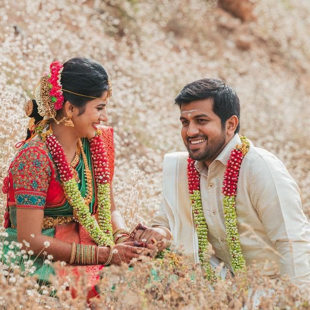 A smiling couple in traditional wedding attire, seated among white flowers